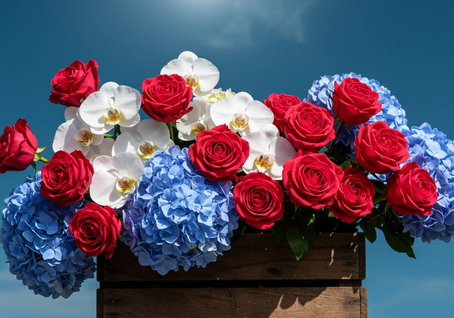 Red roses, white orchids, and blue hydrangeas arranged in a wooden planter, showing a bold Patriotic floral arrangement.