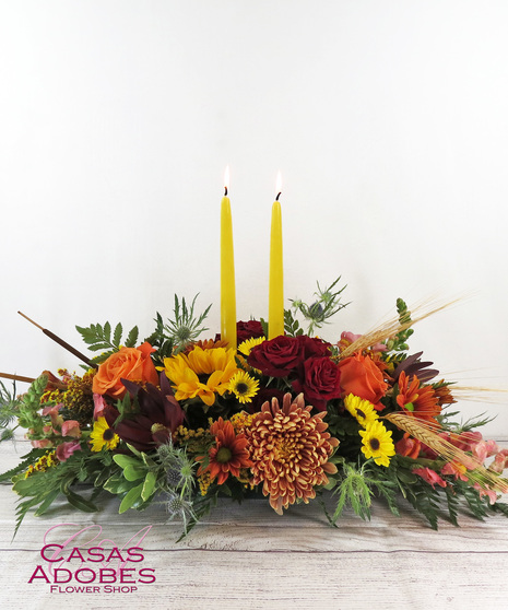 Centerpiece with yellow sunflowers, bronze mums, red roses, orange roses, safari sunsets, wheat, cattails and more fall color flowers. 2 taper candles included.