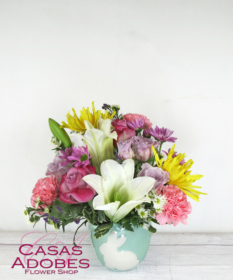 Bunny container with white lilies, yellow mums, lavender roses, pink carnations and monte casino