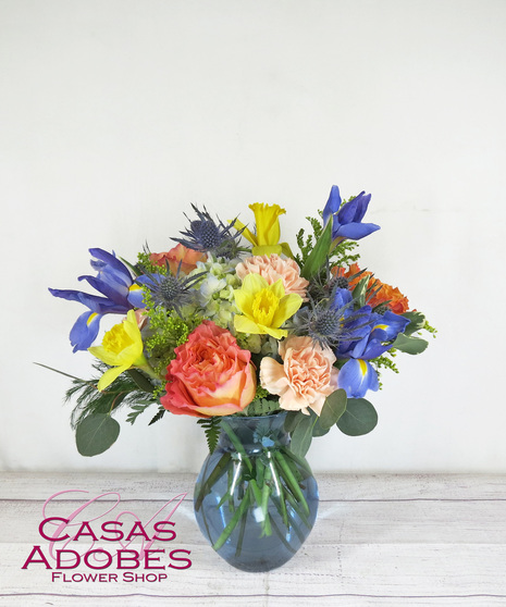 Blue vase with blue iris, thistle, daffodils, peach carnations, coral roses and hydrangea