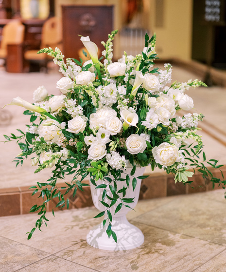 altar arrangement featuring peonies, white roses, calla lilies, white lisianthus, snapdragons, and filled with greenery in a gorgeous urn.