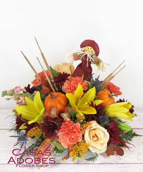 centerpiece with fall flowers, including carnations, lily, thistle, chrysanthemums in fall colors, faux pumpkins, leaves, cattails, cute scarecrow pick