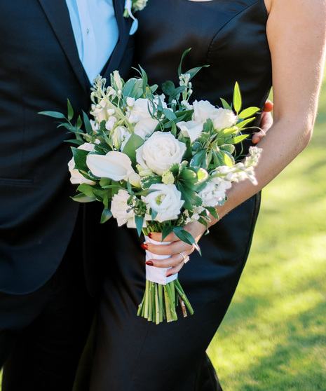 A loose hand-tied bouquet featuring all-white roses, miniature calla lilies, stock, lisianthus and ruscus.