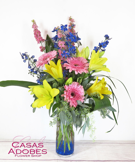 Vase with blue delphinium and yellow lilies and pink gerbera daisies