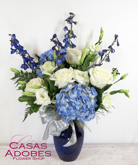 Blue vase filled with blue and white flowers, including white roses, blue hydrangea, and blue delphinium