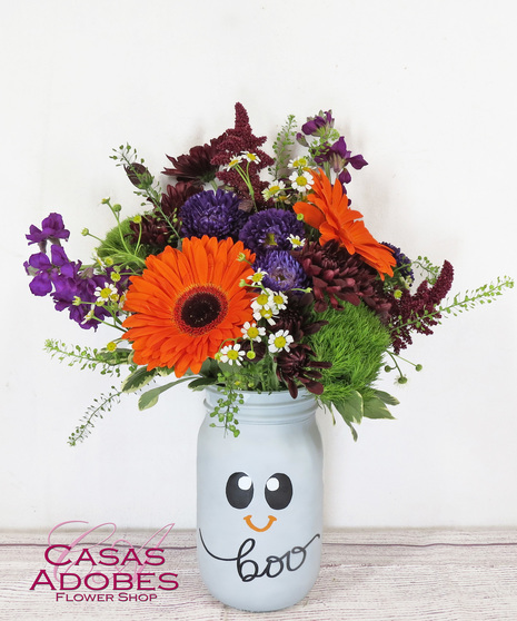  Marigolds, orange lily, berries, solid aster and statice in an orange pail with a jack o lantern face with birch branches and faux spiders
