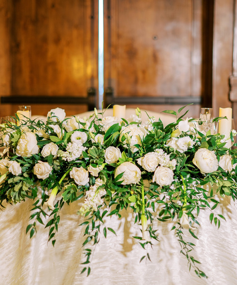 large centerpiece featuring peonies, white roses, white miniature calla lilies, white lisianthus, white stock, and filled with greenery. 