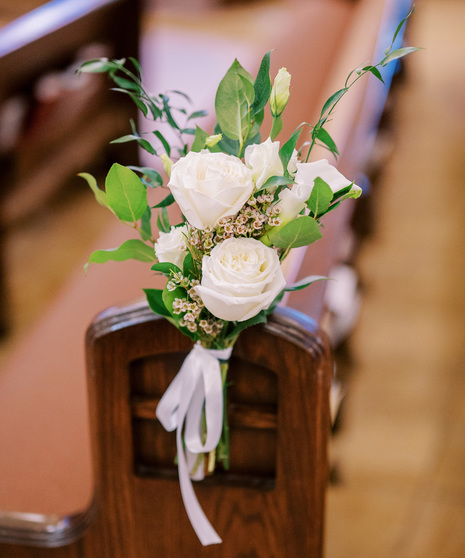 aisle (pew) bouquet featuring white roses, miniature calla lily, waxflower, and touch of greenery with a delicate ribbon.