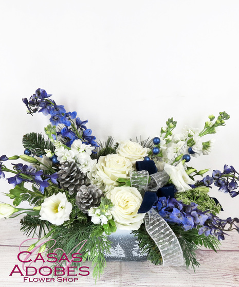 Snowy pine planter with white roses, white lisianthus, blue delphinium, pine cones, winter greens and velvet and silver ribbon