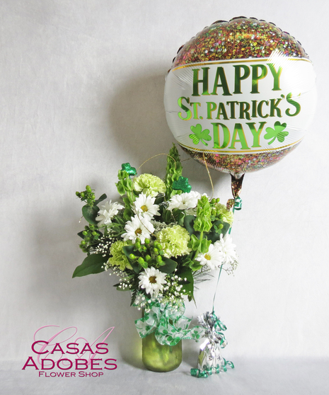Bells of Ireland, green carnations, green coffee berry, white daisy  with gold ting ting and sparkling shamrock picks in a green mason jar with a shamrock bow. 